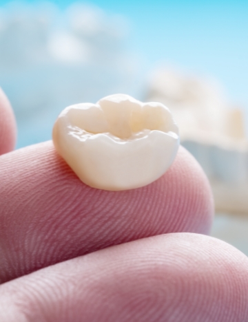 Close up of a dental crown resting on a person's finger